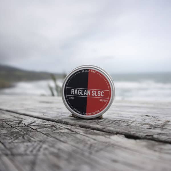 Outdoor Raglan Surf Lifesaving zinc sunscreen on weathered wooden surface with ocean in background, promoting sun protection and safety at Raglan surf beaches in NZ.