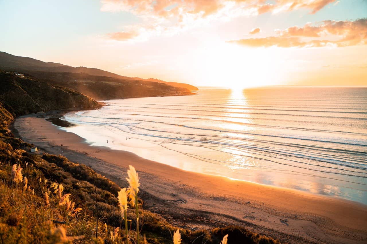 Golden sunset over Raglan Beach with calm surf and scenic coastline, showcasing Surf Lifesaving activity in New Zealand's popular coastal destination.